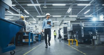 Engineer inspecting factory with tablet and helmet.