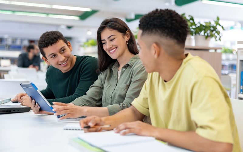 Happy group of Latin American students studying at the library using a digital tablet - education concepts