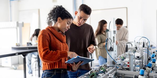 Two students working on a robotics project with a tablet in a lab.