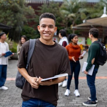 Joven sonriente con cuaderno en campus universitario.