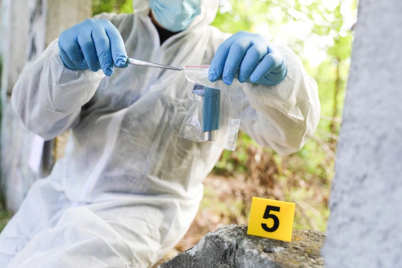 A forensic scientist in protective gear working on site during a crime scene investigation. Collecting, analyzing, and documenting evidence in an outdoor environment using professional tools and sterile techniques. The image depicts a typical moment of criminal investigation in real-life conditions.