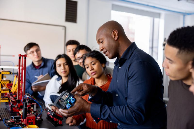 African American teacher showing a model to a group of students while teaching a robotics class