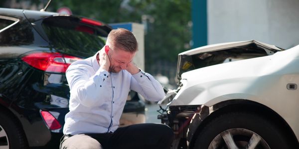 Man in white shirt holding his neck in pain near damaged cars after accident.