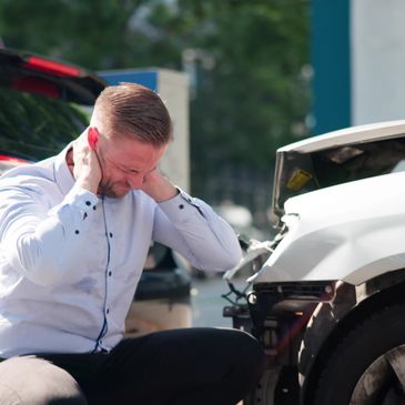 Man in pain near a damaged car after an accident.