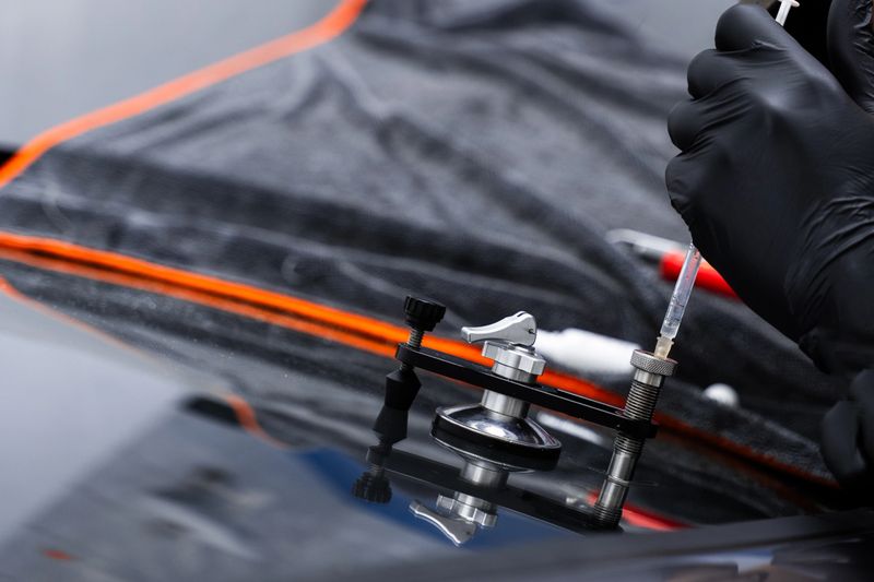 Resin repair on windshield using injector application to restore structural clarity. Windshield crack repair using resin injection. Technician using windshield injector tool to fix bullseye crack