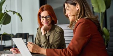 Two women collaborating over a laptop in a modern office.