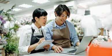 Two florists working together using a laptop and notebook in a flower shop.