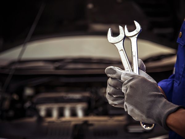 Rutland Mechanic holding two wrenches in front of a car engine.