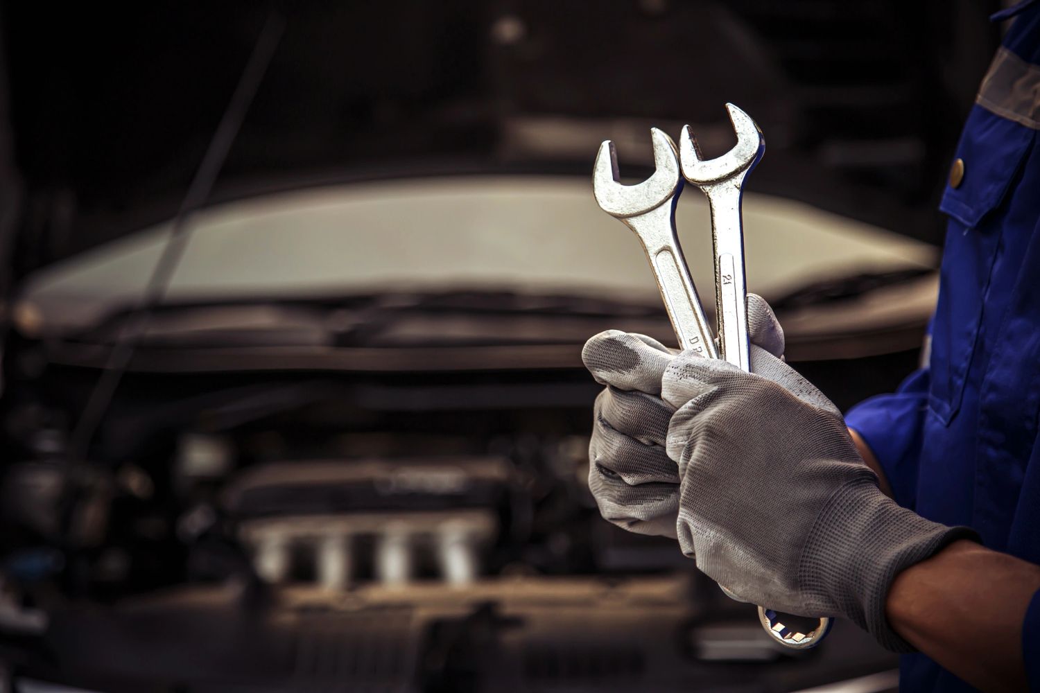 Mechanic holding wrenches near a car engine.
