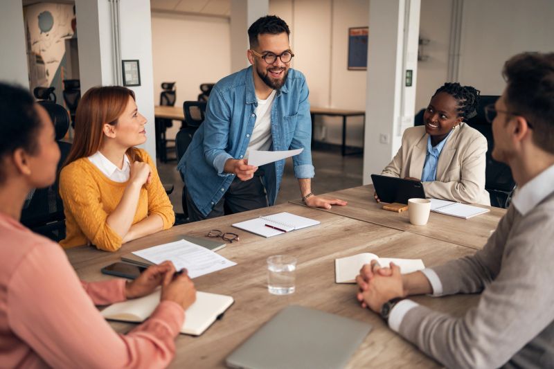 A diverse workplace team gathered around a meeting table discussing ideas, showing collaboration, engagement, and teamwork in a professional environment. Ideal for showcasing modern business dynamics.