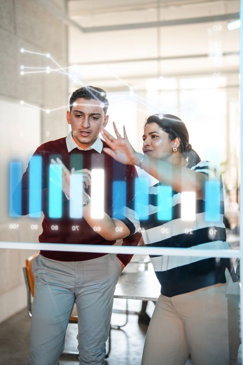 Portrait shot of young Hispanic male executive and mid-adult Indian female colleague collaborating on transparent holographic interface in contemporary corporate office environment.