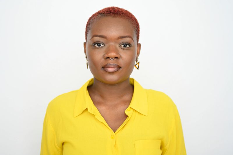30s female with short hair and confident expression wearing a bright yellow shirt against a plain background
