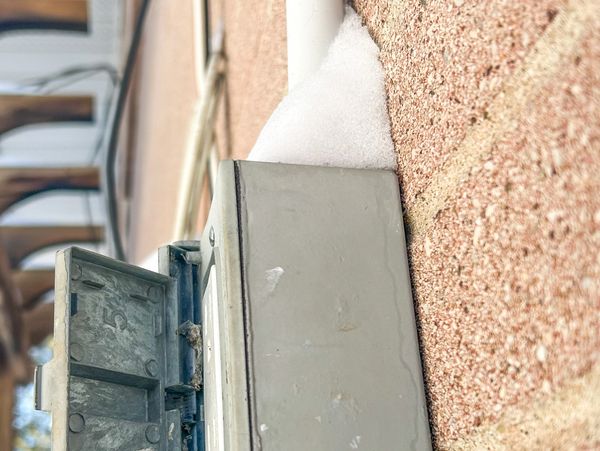 Close-up of a metal utility box mounted on a brick wall with some snow on top.