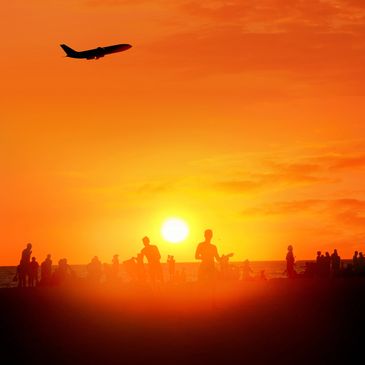 Silhouettes of people at the beach during a vibrant orange sunset with a plane flying overhead.