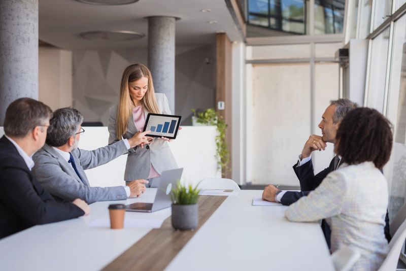 Businesswoman presenting positive data on a tablet during a meeting with colleagues