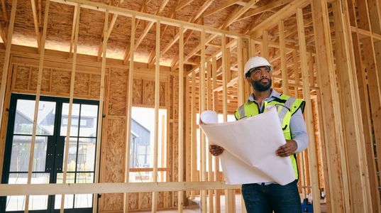 Architectural plans with a white hard hat and drafting tools on a table.