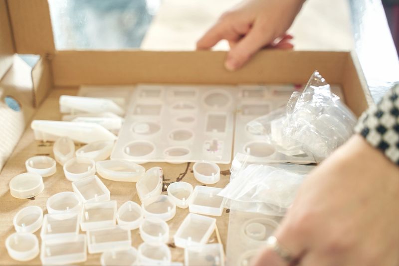 Hands crafting jewelry with silicone molds and resin in artistic workspace.