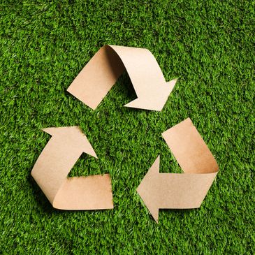 Recycling symbol made from brown paper on green grass.