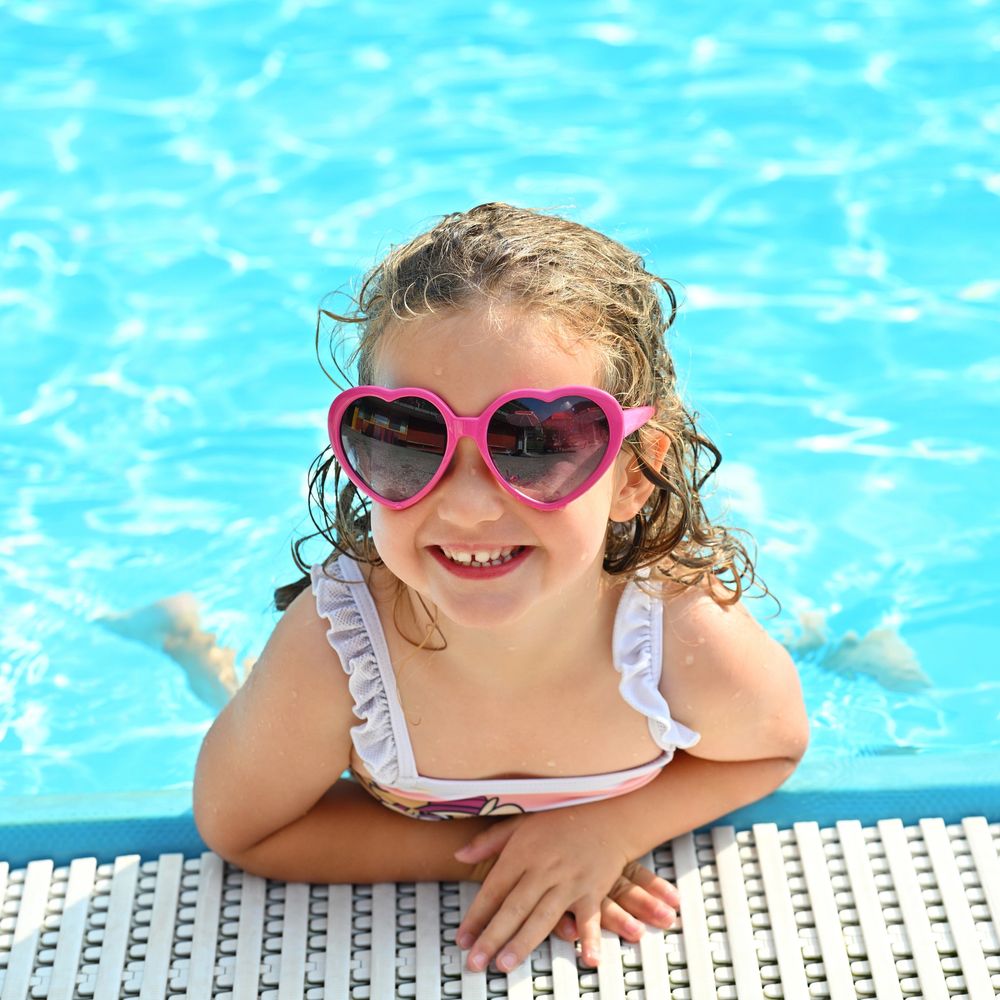 Smiling young girl in heart-shaped sunglasses enjoying a pool day.