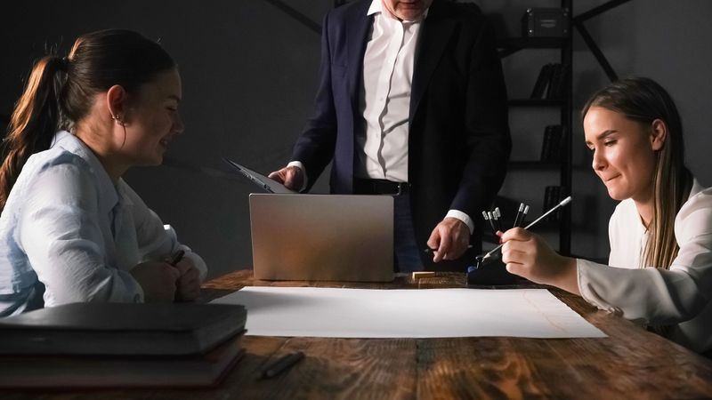 Two women collaborate with a man in a stylish office space, using notes and sketches for ideas.