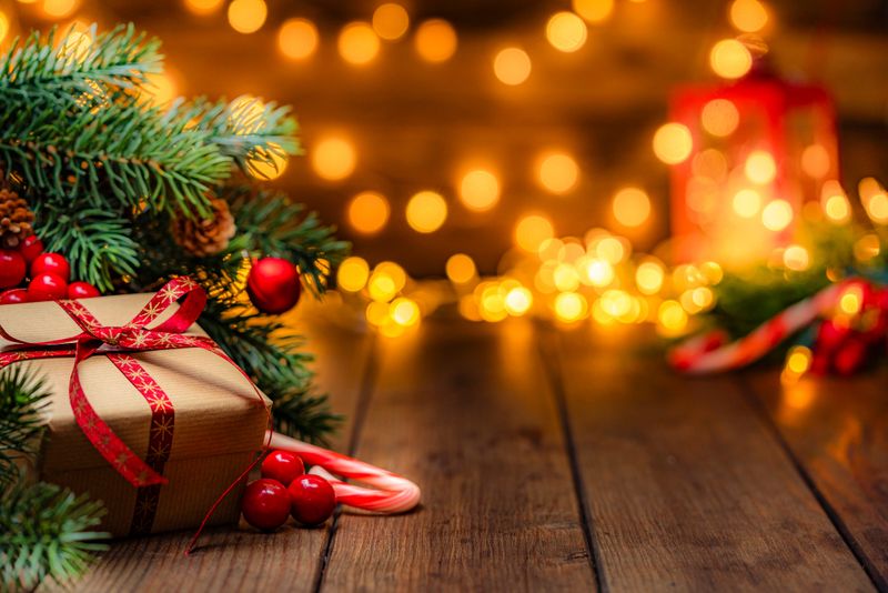 Christmas present wrapped with craft paper and red ribbon under the Christmas tree in a cozy festive atmosphere with defocused Christmas lights at background