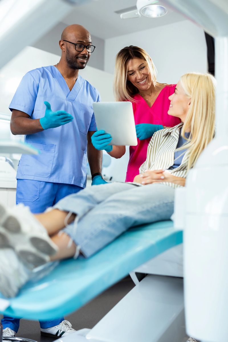 Dentist and nurse showing information on digital tablet to patient lying on dentist chair