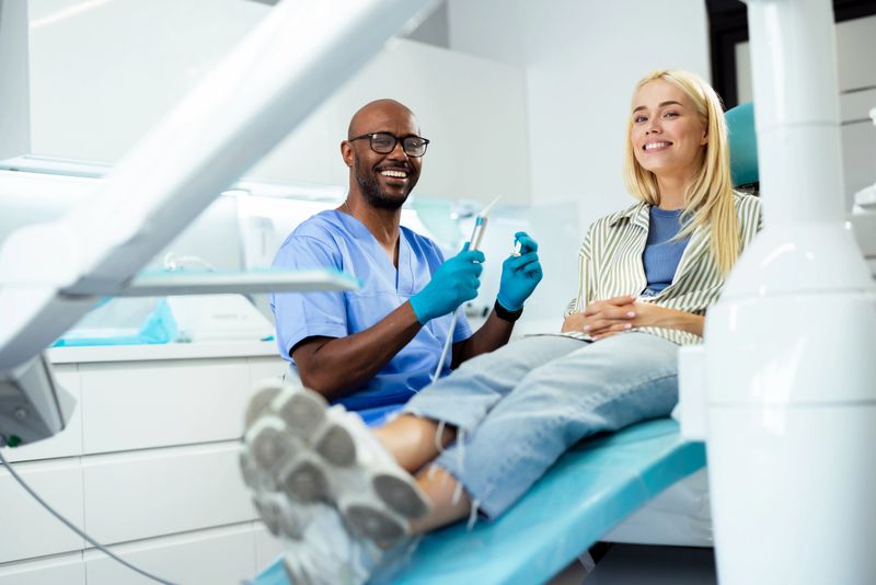 Cheerful dentist holding dental tools and talking to a patient in a dental clinic