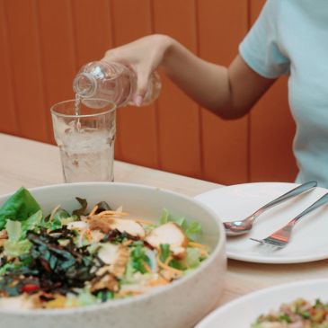 Pouring water into a glass beside a fresh salad.