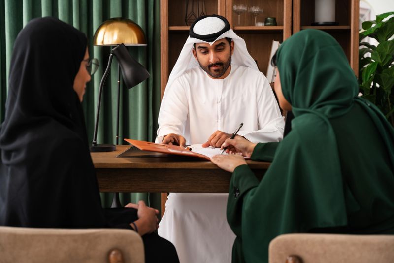 Emirati consultant is guiding clients through a contract signing in a contemporary office setting, fostering trust and expertise in financial matters