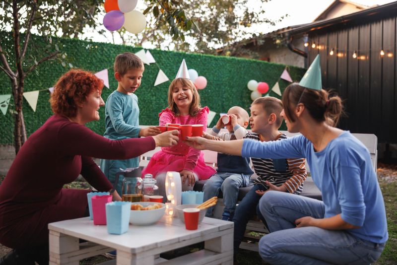 Children having fun at an outdoor playground birthday party, taking a break from playing for snacks and juices, making a toast with birthday girl