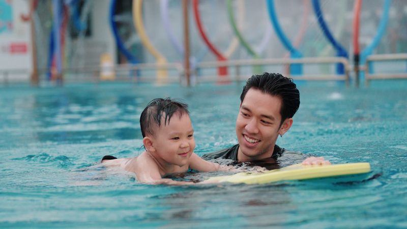 Older brother teaching his little brother to swim in the swimming pool.