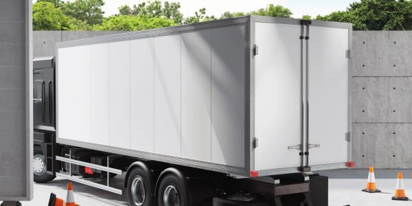 A white cargo truck parked near a concrete wall with traffic cones around.