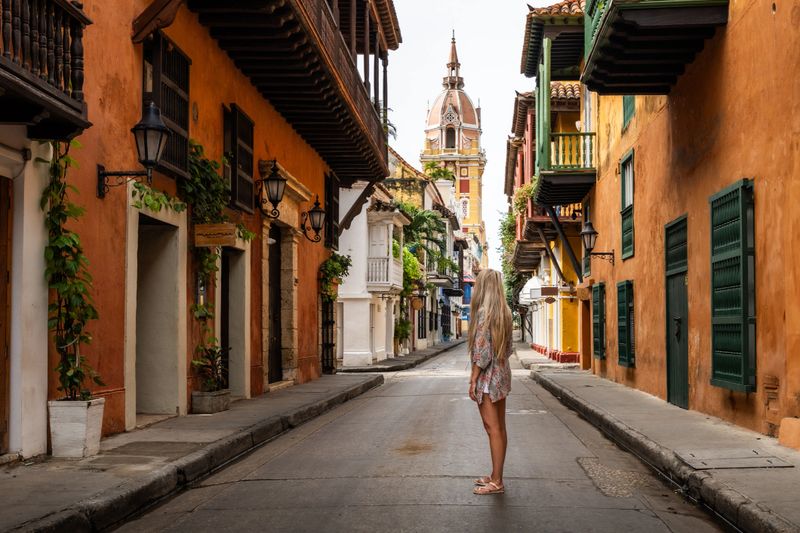 Blonde tourist standing in the middle of a street admiring the colorful colonial architecture of cartagena de indias