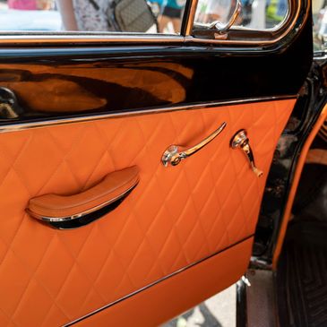 Vintage car door panel with orange quilted leather and chrome handles.
