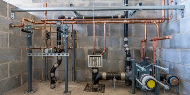 Industrial plumbing system with copper pipes and machinery in a concrete room.