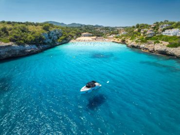 A boat floats on clear blue water near a sandy beach and green hills.