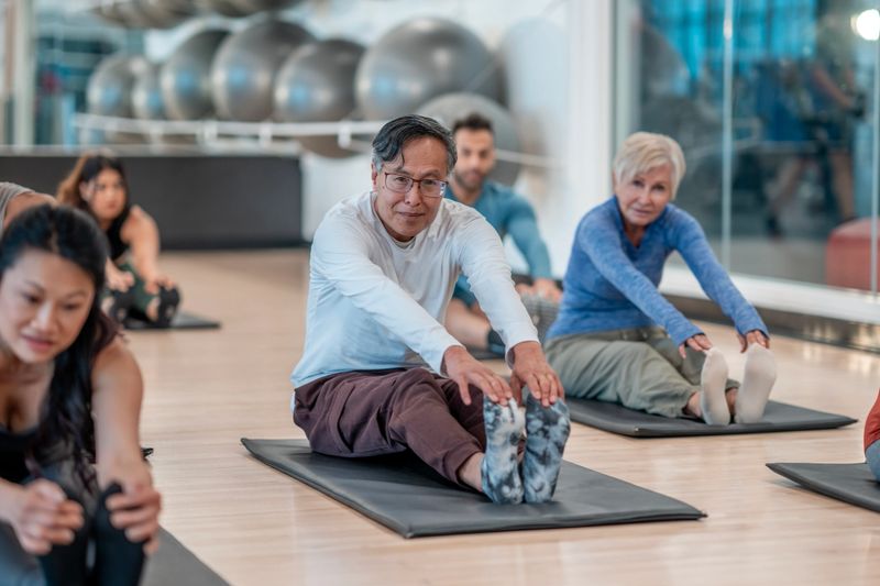 A diverse group of adults participate in a fitness class, stretching on mats. The relaxed and uplifting atmosphere promotes health, wellness, and community. The setting is a well-equipped fitness facility.