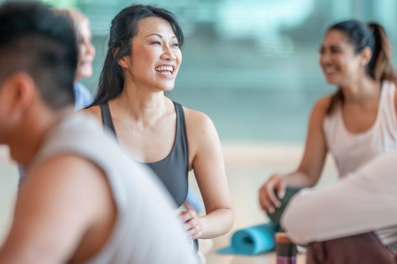 A group of people gather and interact during a friendly yoga class, fostering joy and positive energy in a vibrant, supportive atmosphere. They share laughter, cultivating wellness and a sense of community.