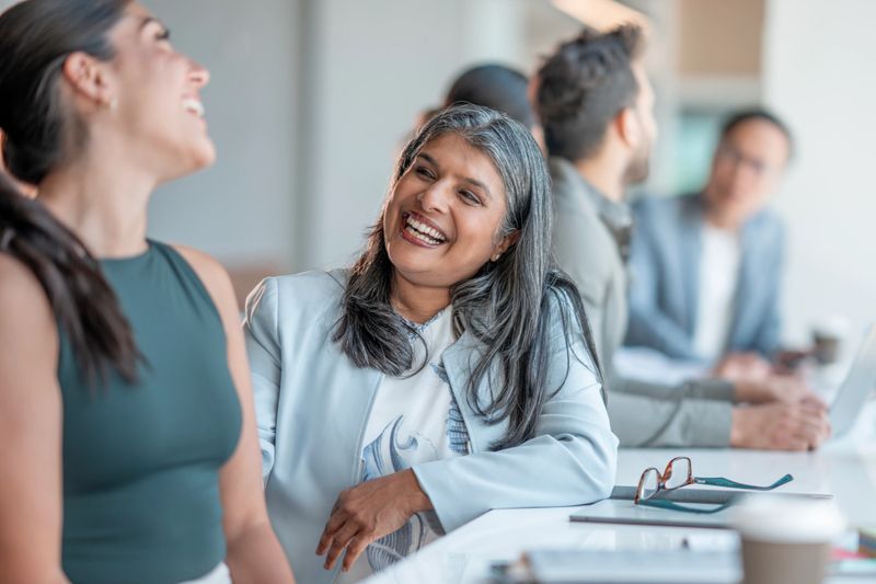 Group of diverse colleagues having a cheerful and engaging conversation around a conference table. Focusing on teamwork, collaboration, and a positive workplace atmosphere.