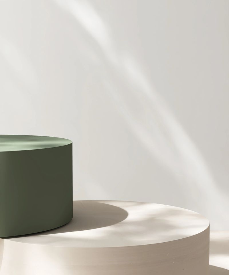 Minimal, modern cream and green round pedestal podium table in foliage dappled sunlight on white wall for luxury, elegant cosmetic, skincare, body care, beauty product display background 3D