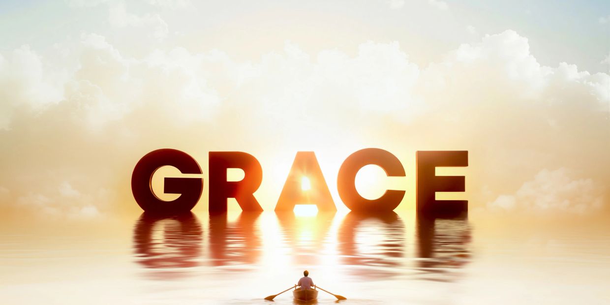 A person rowing a boat toward large letters spelling GRACE at sunrise.