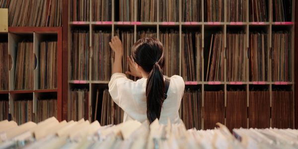 Pessoa examinando uma grande coleção de discos de vinil em um quarto aconchegante.