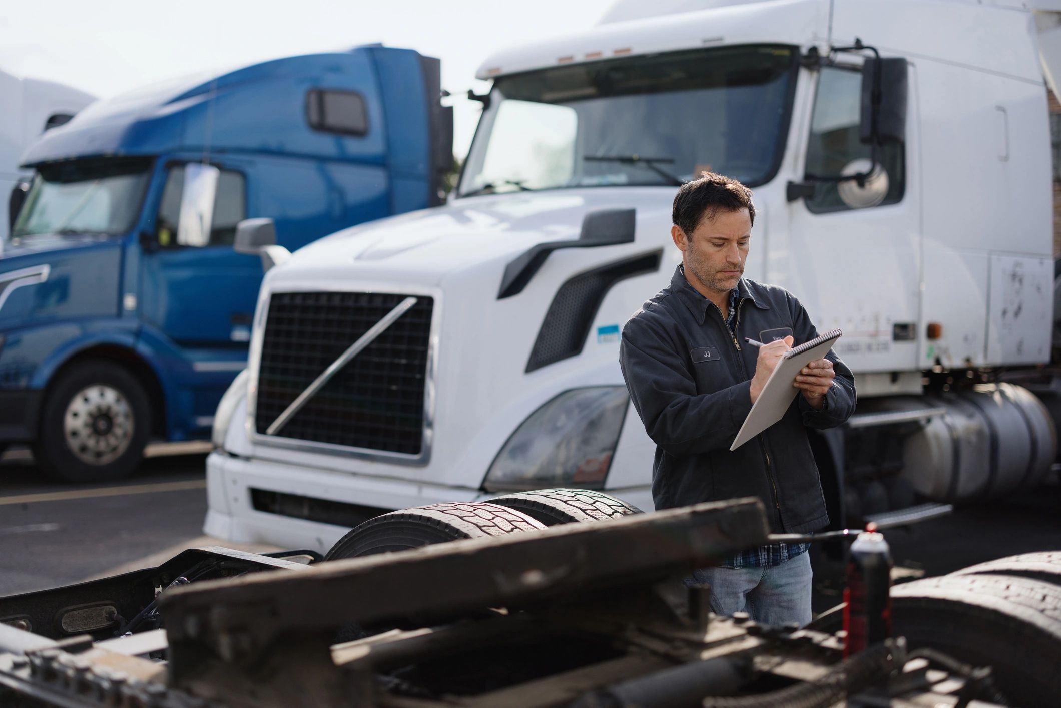 Mechanic inspecting and taking notes on a white semi truck in a truck yard.