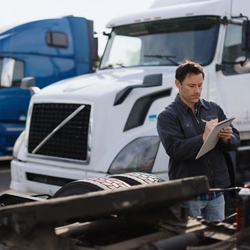 Mechanic inspecting and taking notes on a white semi truck in a truck yard.