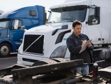 Mechanic inspecting and taking notes on a white semi truck in a truck yard.