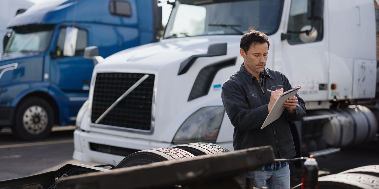 A man inspects and takes notes beside a white semi-truck in a parking area.