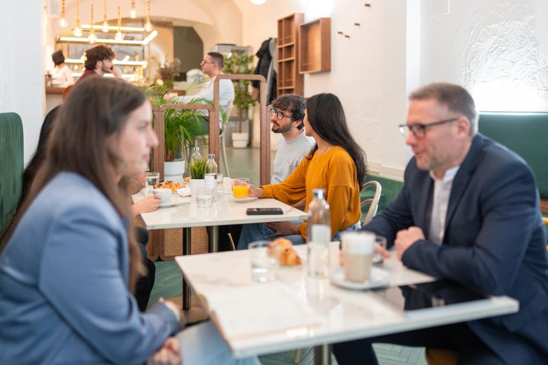 A cozy bistro with diverse guests, including men and women, enjoying drinks and casual conversations. Bright modern interior with natural light and stylish decor enhances the atmosphere.