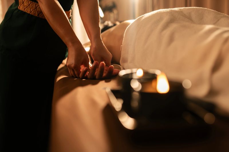 Thai therapist performing hand massage with warm oil from melted massage candle. Soft lighting and cozy spa setup create a serene, therapeutic wellness atmosphere.