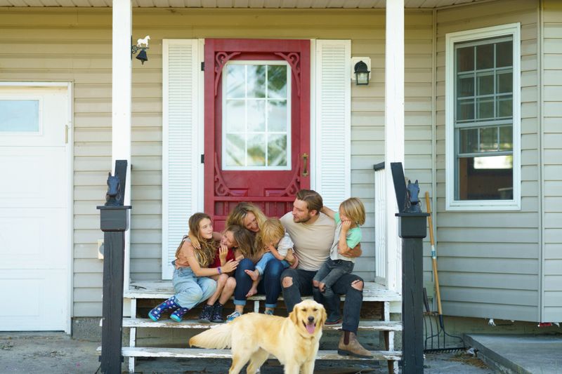 A cheerful family spending quality time together outdoors on their porch, with their friendly golden retriever. Warm surroundings and bright smiles convey togetherness and a peaceful lifestyle at home.