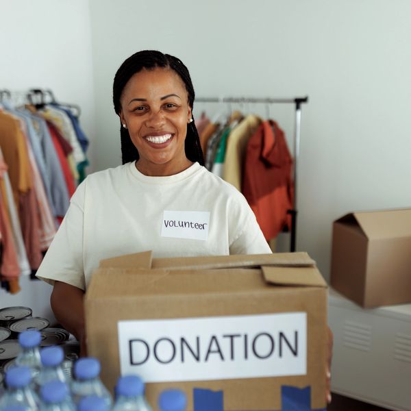Smiling volunteer holding a donation box surrounded by canned goods and clothes.